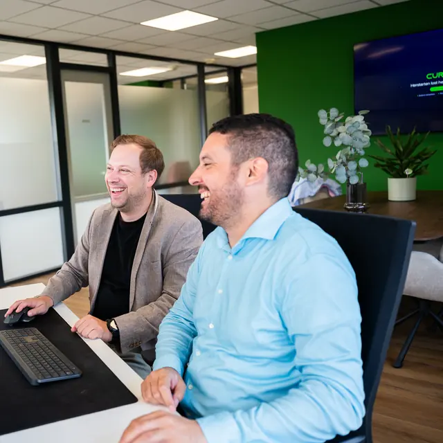 Twee collega's van Cura ICT in een vrolijk gesprek op kantoor