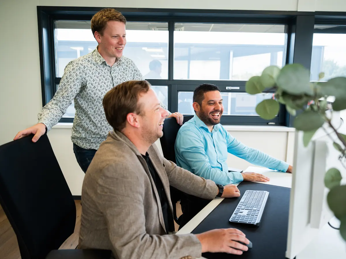 Drie collega's van Cura ICT lachen samen achter een bureau